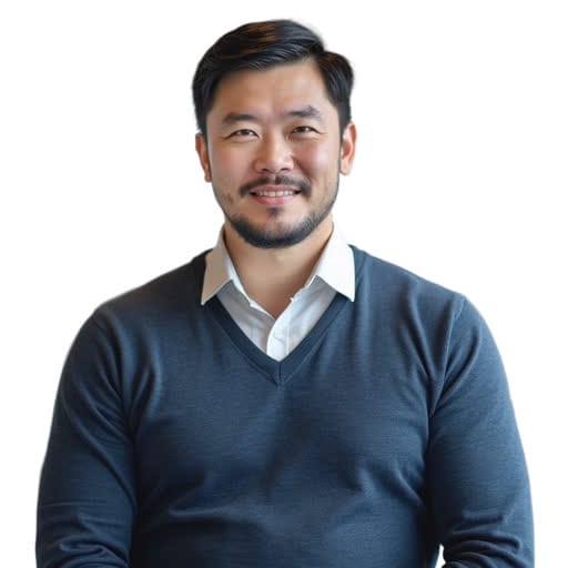 A man with short dark hair and a beard is smiling, wearing a white shirt and a dark pullover, standing against a plain white background.