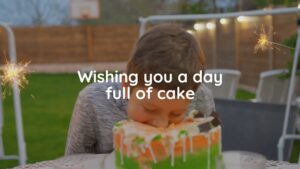 A boy bites into a cake with sparklers lit on top at an outdoor birthday celebration, with the text "wishing you a day full of cake" created using Biteable video maker overlaying the