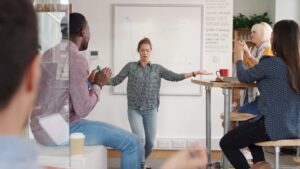 A group of individuals engaged in a team meeting with one person presenting a Biteable video maker project in front of a whiteboard.