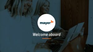 Two colleagues sharing a light moment beside a laptop in an office setting, with a "welcome aboard" message from Mayer featuring Biteable video maker.