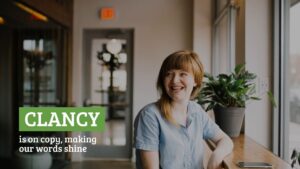 Smiling woman with short blonde hair, wearing a blue shirt, seated at a table in a cafe with the text "Biteable video maker, making our words shine" overlayed.