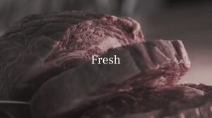 Close-up of raw, sliced beef with the word "Fresh" overlaid in white text at the center—ideal for a restaurant ad video template.