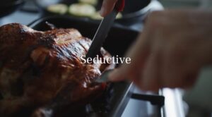 A hand carves a roast chicken in a pan, with the word "Seductive" overlaid in white text at the center—a perfect restaurant ad video template.