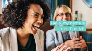 Two women in business attire are having a conversation; one is smiling broadly. Text overlay reads, "Hello, my name is Lauren Cundall.