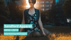 A person in a floral dress sits on grass at sunset in an urban park. Text overlay reads: "Sandford Apparel, 2016–2019, Marketing Manager.