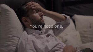 A man resting in bed with his hand on his forehead, accompanied by the Biteable video maker text "you're not alone.