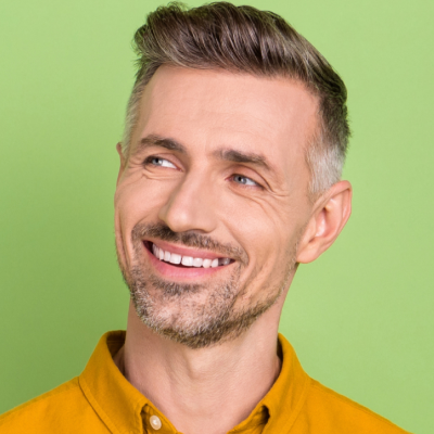 A smiling middle-aged man with short gray hair, wearing a yellow shirt, against a green background.