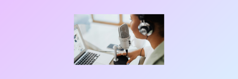 Person wearing headphones speaks into a microphone while looking at a laptop screen on a desk.